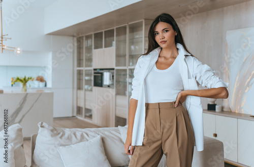 gorgeous Asian Fashion model is standing home in trousers, looking at camera with a serious face. Household chores , women home. Domestic leisure, weekend.