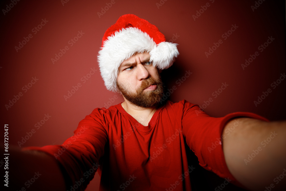 Close Portrait of bearded Santa Claus in red hat, white beard with pensive emotion on red background Close Portrait of bearded Santa Claus in red hat, white beard with pensive emotion on red background