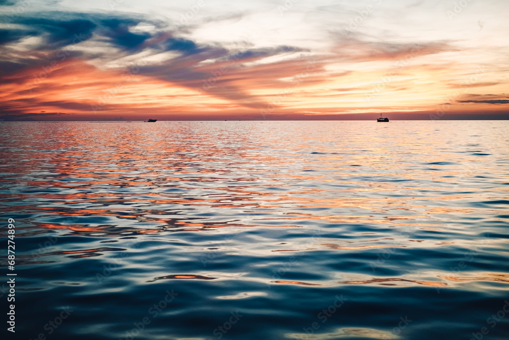 As the fiery sun dips below the horizon, a tranquil lake mirrors the painted sky, with boats bobbing gently in the water, creating a symphony of nature's beauty and serenity As the fiery sun dips below the horizon, a tranquil lake mirrors the painted sky, with boats bobbing gently in the water, creating a symphony of nature's beauty and serenity
