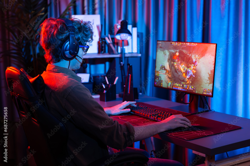 Host channel of young gaming streamer playing fighting Moba at battle arena game with multiplays team, wearing headphone on pc monitor with back side image at neon digital light modern room. Gusher.