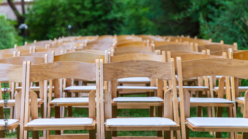 Wooden folding chairs in a garden before an outdoor wedding ceremony.