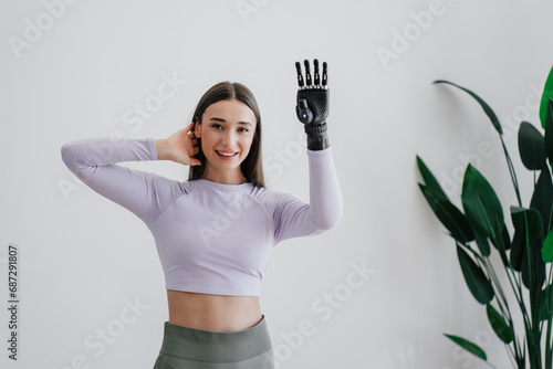 Beautiful European brunette girl in sportswear adjusting hi tech arm prosthesis at home against large plant on background. Orthopaedics and medicine for people after trauma. Hi tech medicine.