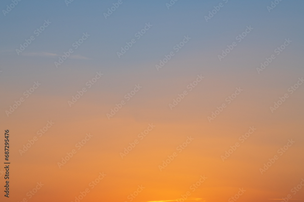 Abstract landscape of a sunset. The evening sky shifts color from orange to dark blue in a smooth gradient, with some faint clouds visible.