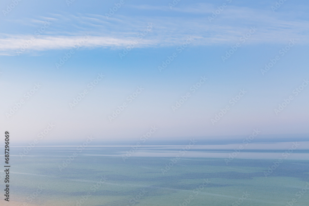 Blue sky with haze and blurry glowing pink clouds above the sea. Shallow coastal sea water with azure patterns. Ripples in the water