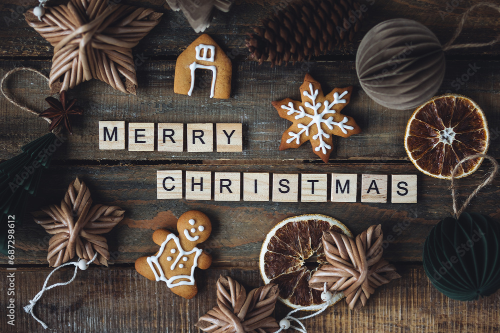 Holidays card on wooden background with gingerbread cookies, handmade craft toys, festive rustic zero waste decorations. Sustainable lifestyle. Merry Christmas greeting written with wooden blocks. Holidays card on wooden background with gingerbread cookies, handmade craft toys, festive rustic zero waste decorations. Sustainable lifestyle. Merry Christmas greeting written with wooden blocks.