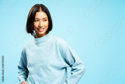 Positive cheerful Asian woman wearing casual clothes looking away posing isolated on blue background