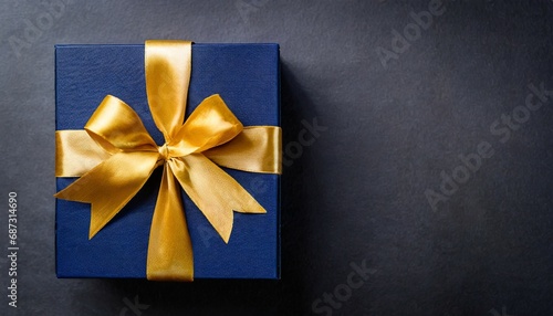 top view of dark blue gift box with gold satin ribbon on dark background top view of birthday gift with copy space for holiday or christmas present