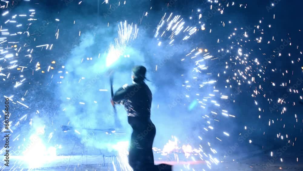 Man in black costume and bandana dances with a stick producing fireworks to the sides. Spectacular fire show at night. Man in black costume and bandana dances with a stick producing fireworks to the sides. Spectacular fire show at night.