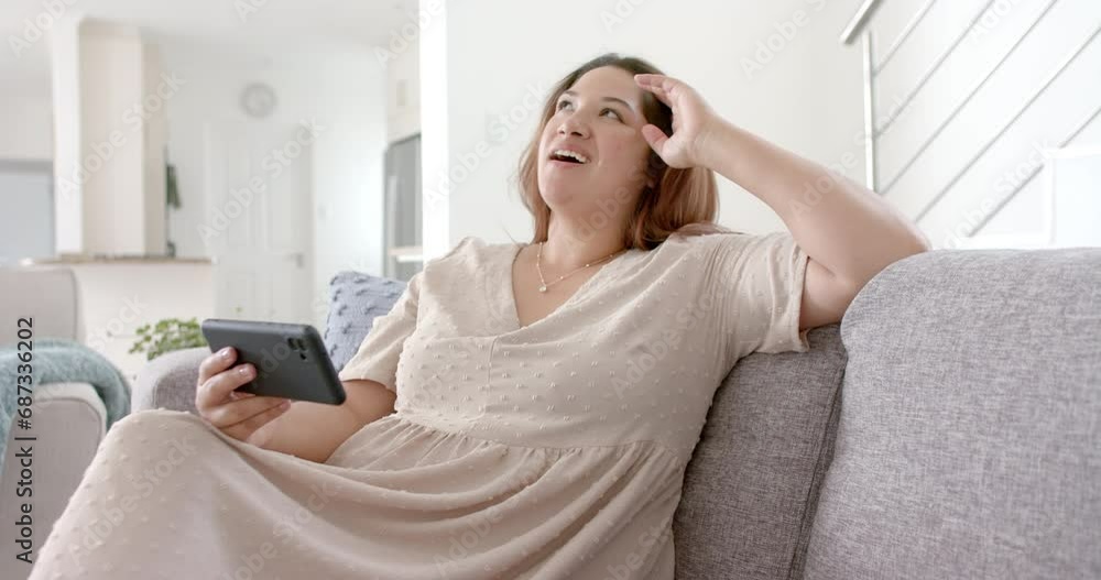 Happy plus size biracial woman having smartphone video call in sunny living room, slow motion Happy plus size biracial woman having smartphone video call in sunny living room, slow motion