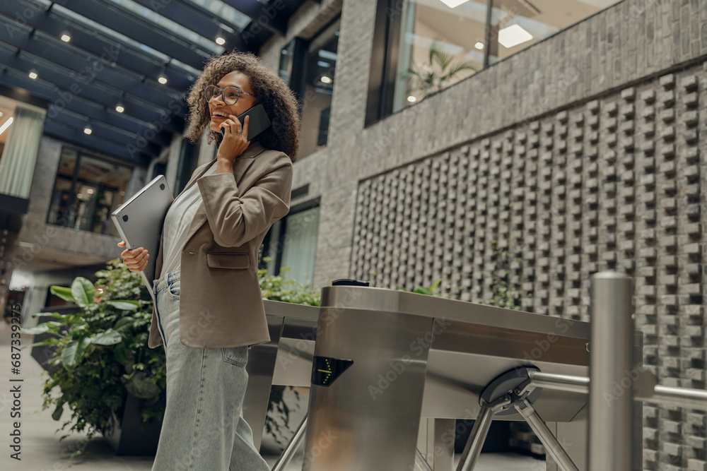 Stylish freelancer is talking phone with client while standing on coworking background Stylish freelancer is talking phone with client while standing on coworking background