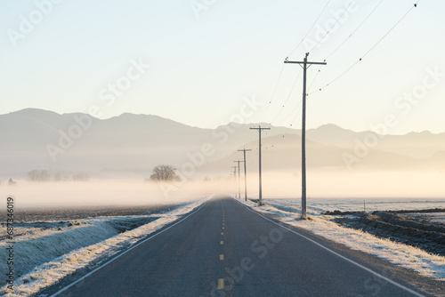 Thin layer of fog across Skagit Valley road at sunrise with telephone poles and lines leading into distance of frosty scene