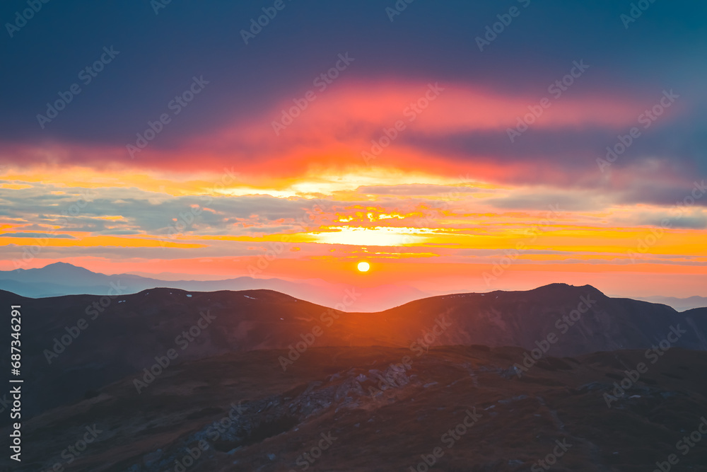 Bright incredible sunset sun over mountain range. Stunning wild nature sunrise. Panoramic view of beautiful mountain landscape. Travel, tourism, adventure, concept image. Carpathian mountains, Ukraine