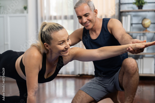 Happy active senior couple in sportswear being supportive and assist on yoga posture together at home. Healthy senior man and woman lifestyle with yoga exercise. Clout