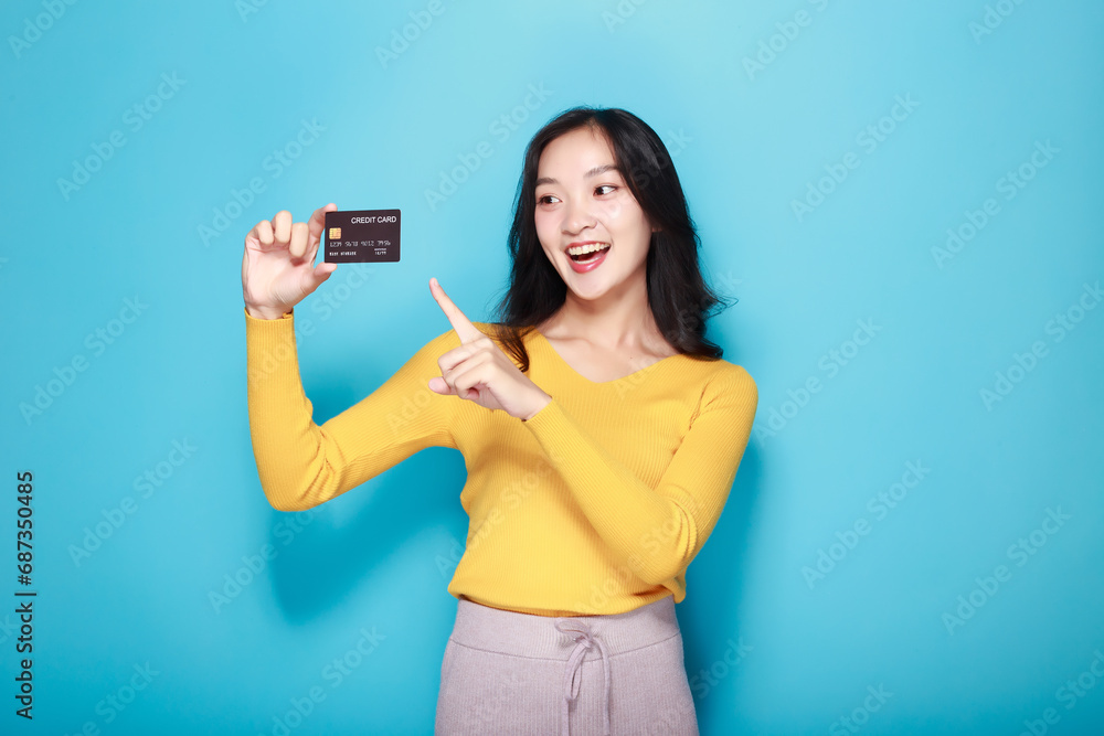 Asian woman posing with a credit card, Portrait of a beautiful young woman in a light blue background, happy and smile, posting in stand position. Asian woman posing with a credit card, Portrait of a beautiful young woman in a light blue background, happy and smile, posting in stand position.