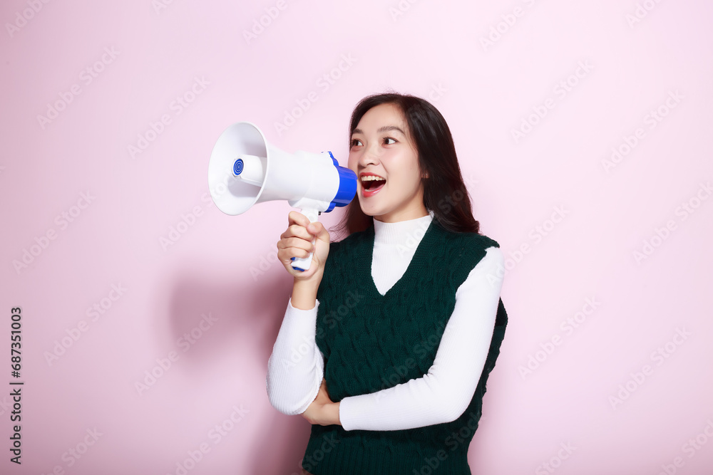 Asian woman posing with a megaphone while standing in front of a light pink background. Asian woman posing with a megaphone while standing in front of a light pink background.