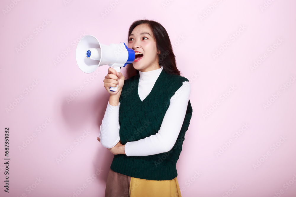 Asian woman posing with a megaphone while standing in front of a light pink background. Asian woman posing with a megaphone while standing in front of a light pink background.