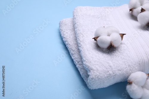 Fluffy cotton flowers and white terry towel on light blue background, closeup. Space for text