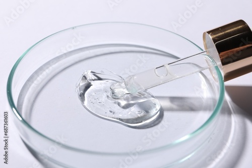 Petri dish with sample of cosmetic serum and pipette on white background, closeup