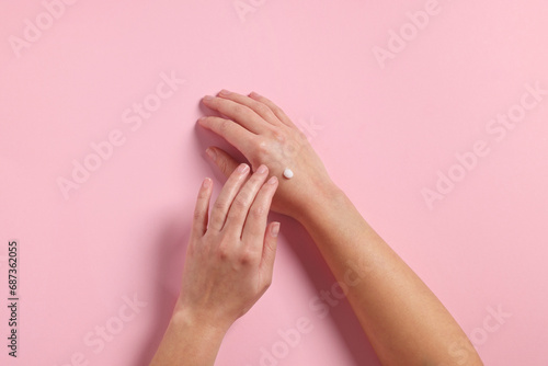 Woman applying cosmetic cream onto hand on pink background  top view