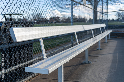An empty aluminum bench in a baseball dugout at a public park.