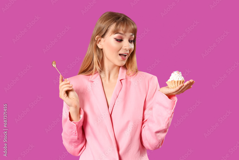 Young woman dressed as doll with cupcake on purple background