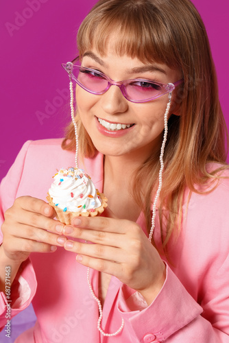 Young woman dressed as doll with cupcake on purple background  closeup