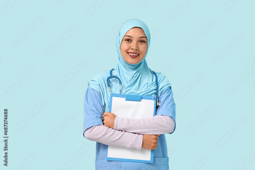 Female Muslim doctor in hijab with clipboard on blue background. World Hijab Day concept Female Muslim doctor in hijab with clipboard on blue background. World Hijab Day concept