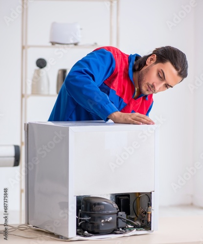 Young male contractor repairing refrigerator at workshop