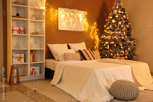 Interior of bedroom with glowing lights, Christmas tree and shelf unit in evening