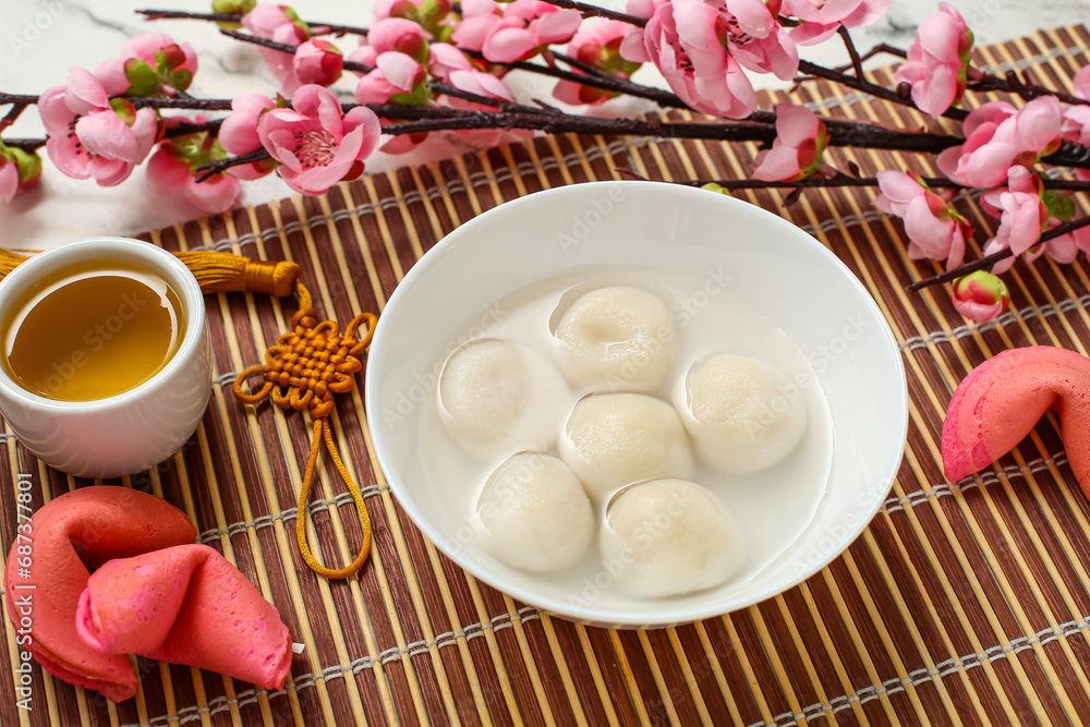 Bamboo mat with bowl of tangyuan, tea, fortune cookies and sakura on white marble background, closeup. Dongzhi Festival Bamboo mat with bowl of tangyuan, tea, fortune cookies and sakura on white marble background, closeup. Dongzhi Festival