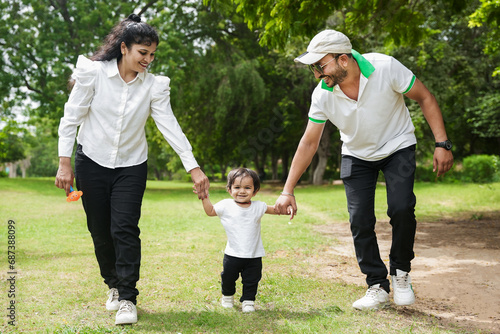 Happy Young indian parents both holding hands of their daughter walking in the park or garden. photo