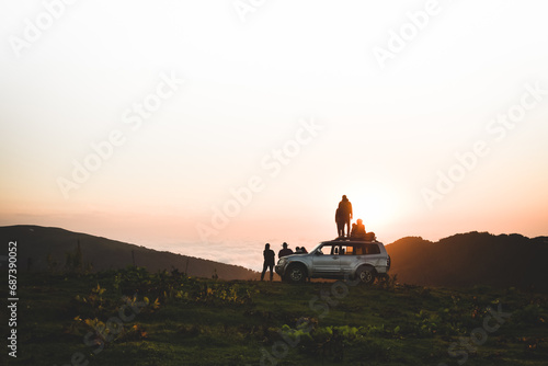 Group of travelers tourist stand by 4wd vehicle together in nature on adventure watch sunset over horizon over cloudscape in wilderness. Exploration and adventure photo
