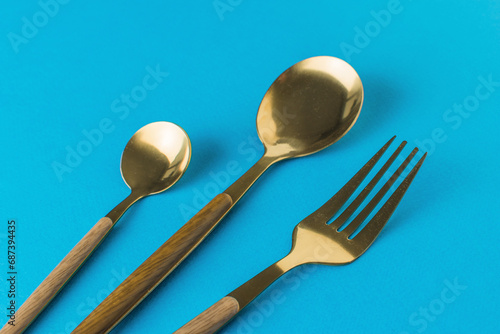 Two gold-plated spoons and a fork on a blue background.