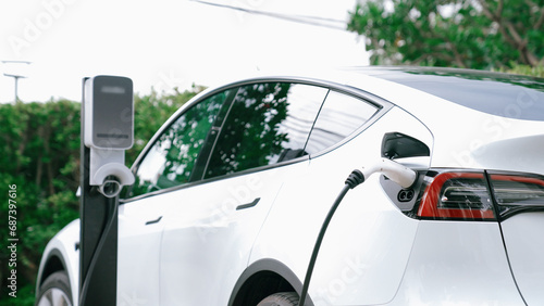 EV electric car recharge battery at parking lot in natural green city park. Alternative clean energy technology for rechargeable automobile for sustainable and eco friendly urban travel. Synchronos