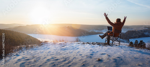 happy man traveler blogger work remote on laptop while enjoying winter nature landscape at sunset.  freedom, travel and remote work concept. banner with copy space.