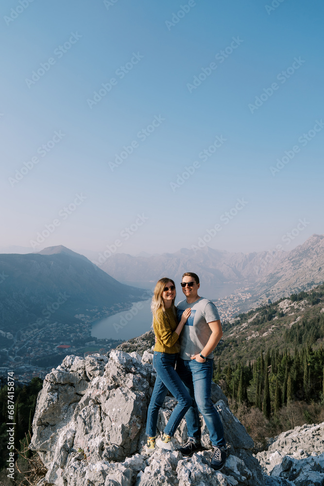 Smiling guy with a girl in sunglasses stands on a rock above the Bay of Kotor. Montenegro