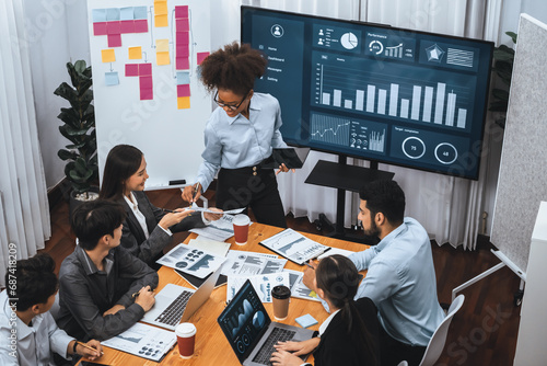 Young african businesswoman presenting data analysis dashboard on TV screen in modern meeting. Business presentation with group of business people in conference room. Concord