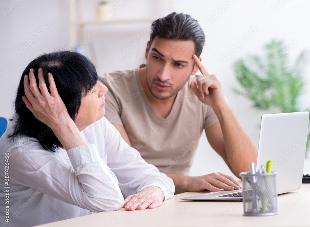 Young male employee explaining to old female colleague how to us Young male employee explaining to old female colleague how to us