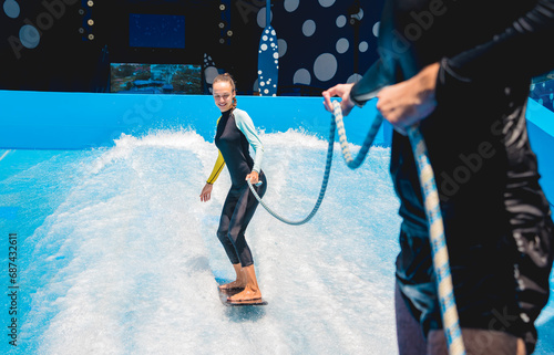 Sticker Beautiful young woman surfing with trainer on a wave simulator at a water amusem