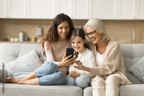 Cheerful mother, grandma and kid using digital gadget, Internet service, online application on smartphone together, enjoying modern technology, communication, leisure at home