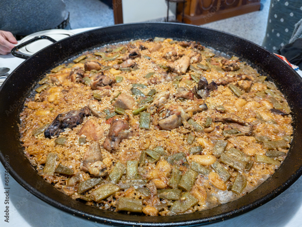 Beautiful and tasty typical Valencian paella made at home, the best-known dish in Spain, on a table and you can see a person placing the plates to eat, typical Spanish tapas Beautiful and tasty typical Valencian paella made at home, the best-known dish in Spain, on a table and you can see a person placing the plates to eat, typical Spanish tapas