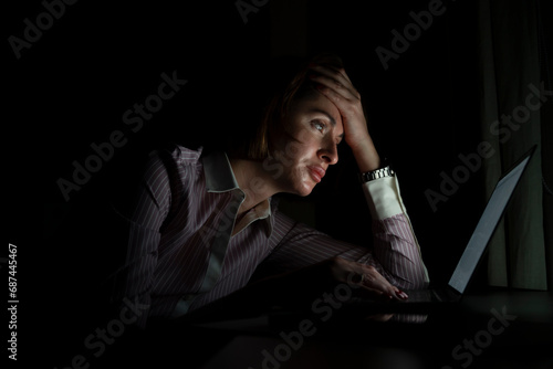 Side view of young tired businesswoman working on laptop at night. Work from home concept photo