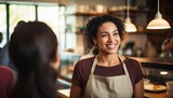 A young black woman with a bright smile in an apron serves customers in a bright cafe.