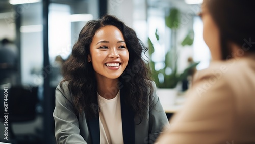 A young Asian woman with long hair smiles while sitting in an office during a meeting. photo