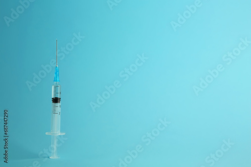 Medical syringe with liquid on light blue background, space for text
