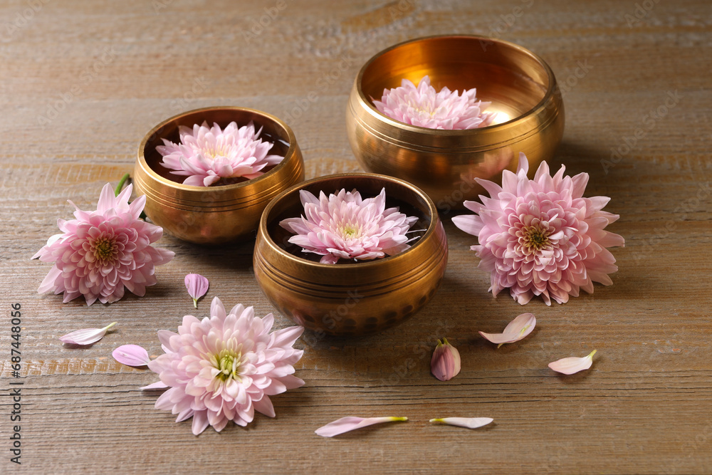 Tibetan singing bowls with water and beautiful flowers on wooden table Tibetan singing bowls with water and beautiful flowers on wooden table