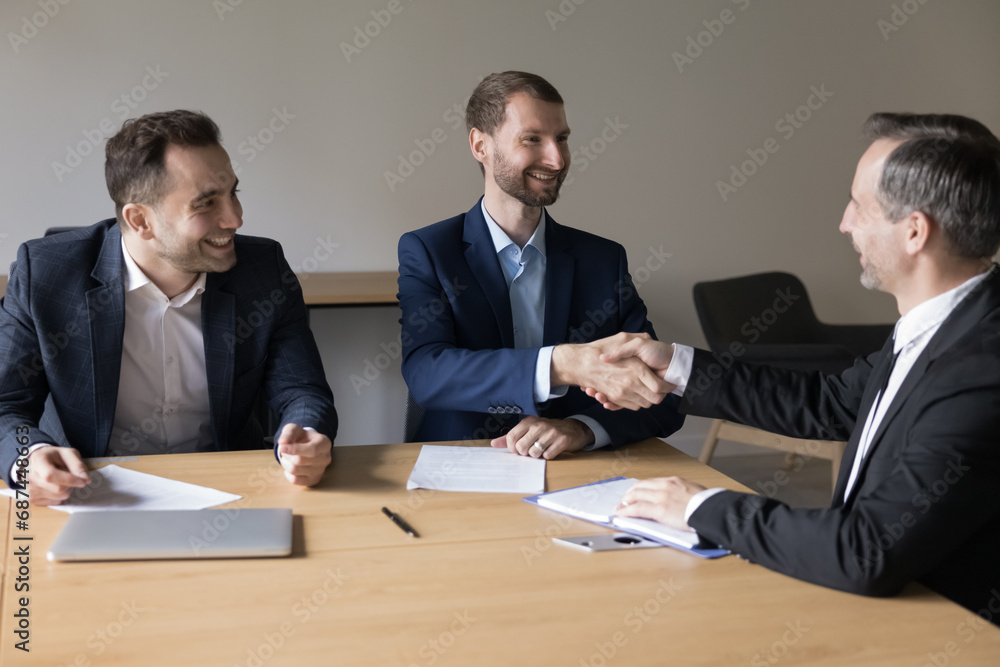 Three satisfied business partners shake hand establish partnership, finish meeting in office conference room. Client and sales managers make deal, handshake, feel satisfied by successful negotiations Three satisfied business partners shake hand establish partnership, finish meeting in office conference room. Client and sales managers make deal, handshake, feel satisfied by successful negotiations