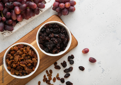 Two bowls with dried raisins with ripe red grapes on light background.Top view.