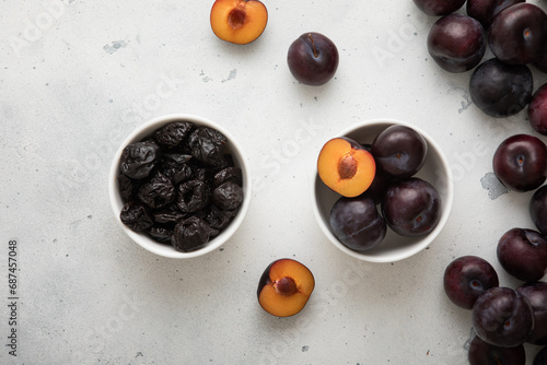 Two bowls with dried prunes and ripe raw plums on light background.Top view.