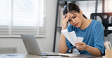 Beautiful asian woman  looking worried over bills while sitting at home office.